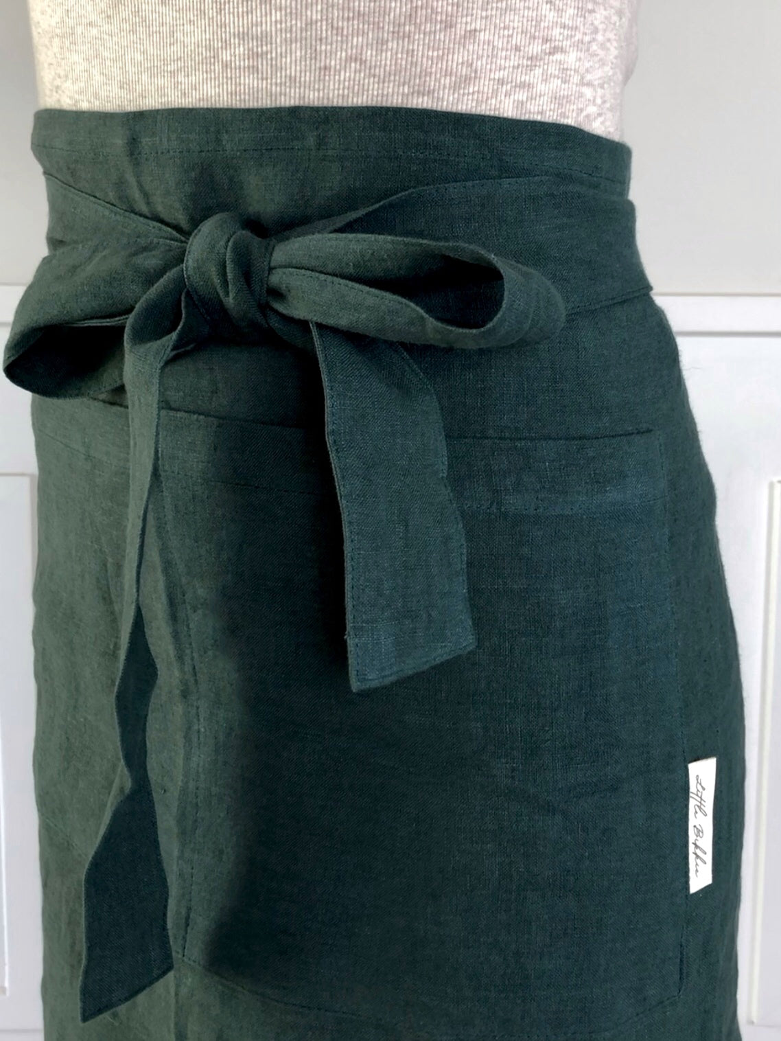 100% linen half waist apron. Large front pocket. Long ties can be fastened at the back or at the front, creating a large bow. Forest green colour way.